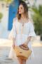 Jeune femme en robe blanche tenant un sac en fibre naturelle fait main par Hamsa, marque artisanale tunisienne.